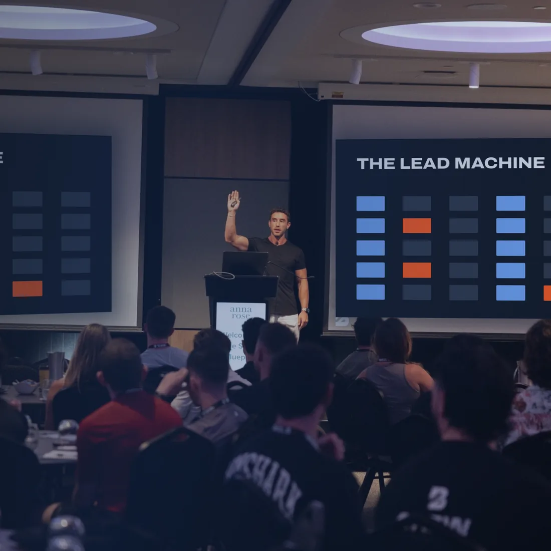 Zac presenting to a full room of coaches at a live Blueprint event, The Lead Machine on the screens behind him
